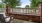 a deck with a bench and a brick wall with trees and a blue sky